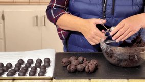 4K HD video of an older caucasian female in kitchen making cake balls with mini meat baller, placing on cutting board, then rolling half of each into balls on cookie sheet.
