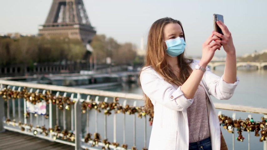 Girl near Eiffel tower in Paris wearing mask and taking selfie or recording video blog during coronavirus outbreak | Shutterstock HD Video #1097398467