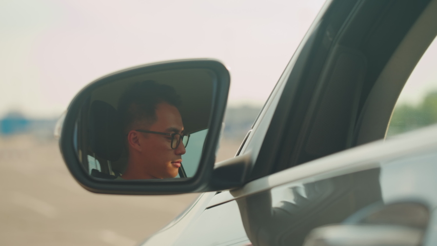 Young Asian Man Driver close-up, Wing Mirror. Car Sharing concept, Vehicle and Transport. Spanish happy guy Driving, sitting in blue car and drinking coffee. Traveling by Automobile. | Shutterstock HD Video #1097401015