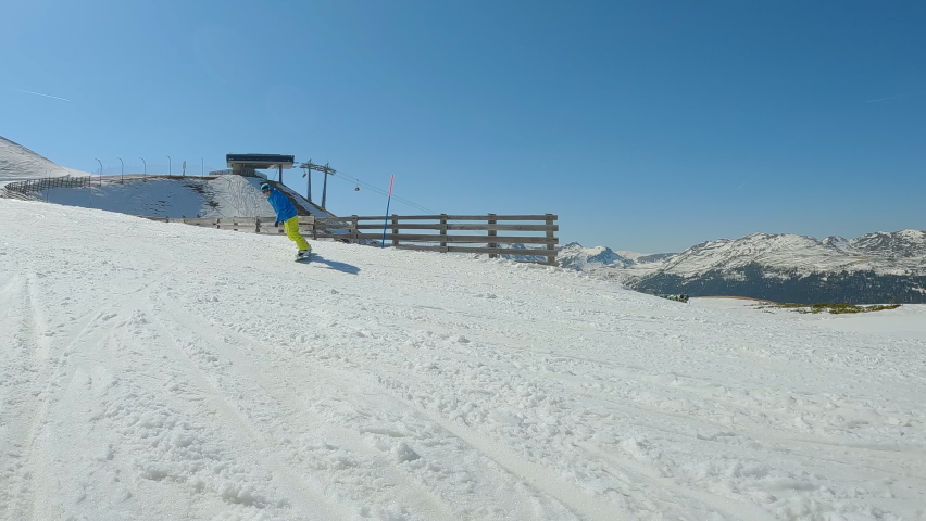 SLOW MOTION: Young man is learning to ride a snowboard when he drops down on snow. Male beginner snowboarder crashes towards camera while making a snowboard turn on slope at snowy mountain ski resort.