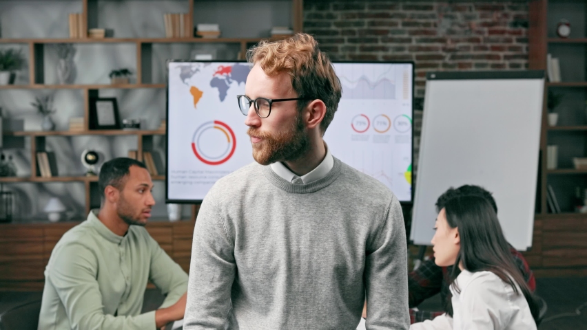Confident smiling ginger guy, startup team leader, standing in front of mixed race office workers or business people with arms crossed or clasped, looking at the camera. business concept | Shutterstock HD Video #1097403561
