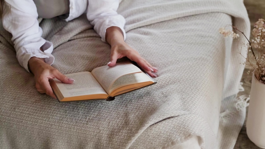Beautiful young woman reading a book on the bed in a cozy bedroom | Shutterstock HD Video #1097407007