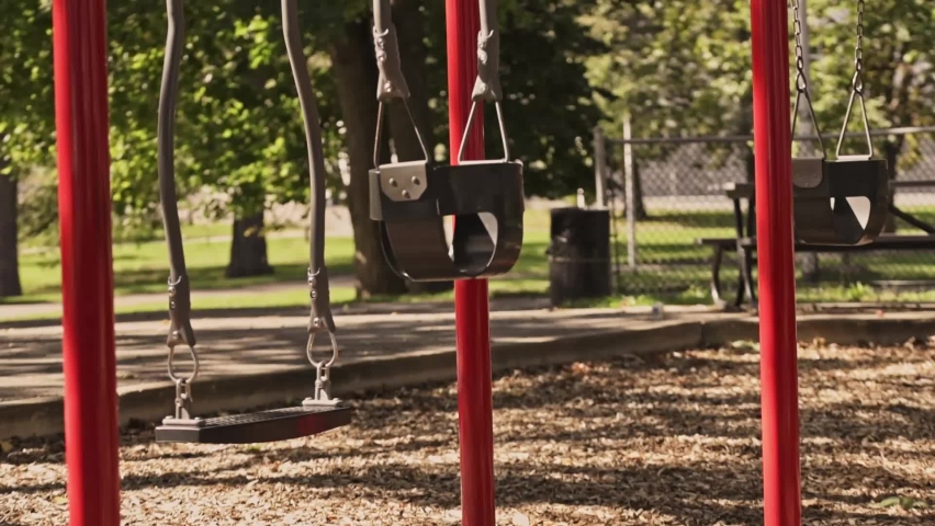 Empty swings slowly moving on the park playground. Summer sunny day. Green trees on the background. Lockdown. Quarantine and isolation | Shutterstock HD Video #1097408777