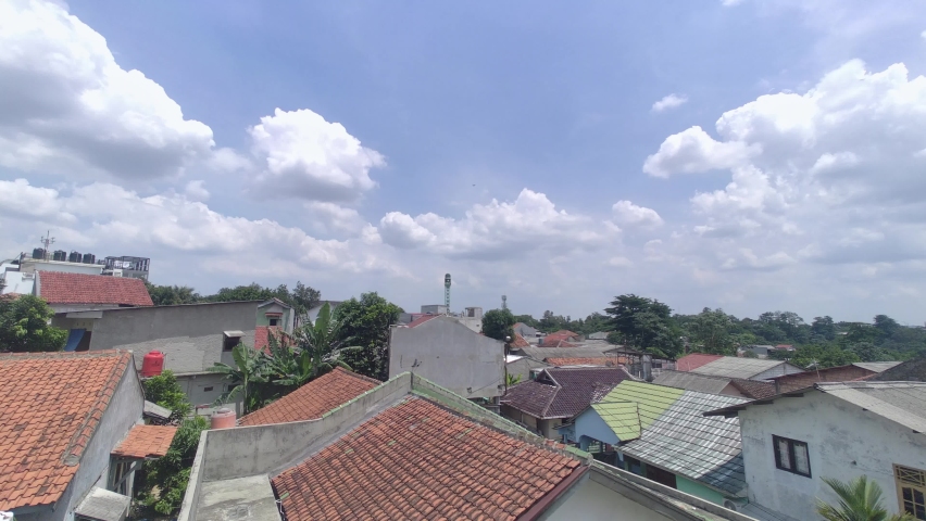 View of blue sky, white clouds, and brown tile roof in suburban area in South Jakarta. Silhouette of an airplane flying in blue sky. | Shutterstock HD Video #1097409331