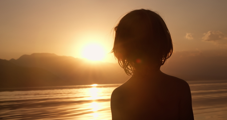 silhouette boy back stands on the shore of the lake child dream childhood memories concept, baby boy child silhouette at sunset at mountains lake sunset time