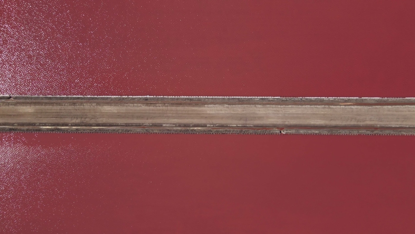 Bright pink lake view from above tracking a long and narrow walk way. 