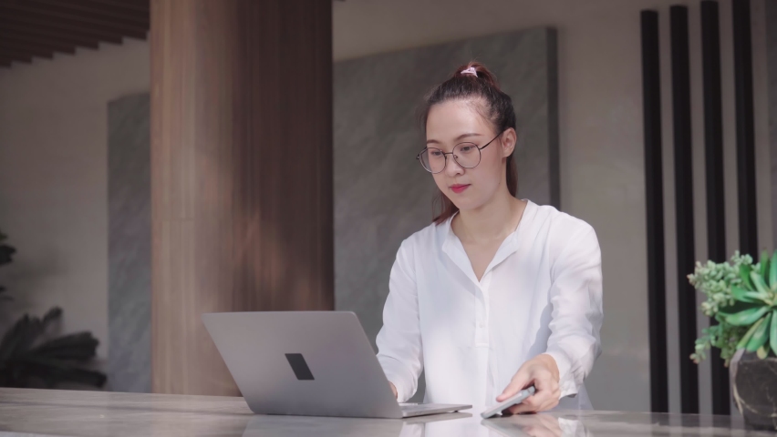 Asian businesswoman talking on the phone talk to business
 while working on a laptop on the table in a modern office at-home coworking space.
 | Shutterstock HD Video #1097414227