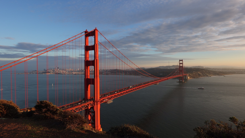 Timelapse of charming city panorama of San Francisco, CA, USA. Busy traffic along Golden Gate Bridge with hilly landscape below cloudy, sunset skyline. High quality 4k footage