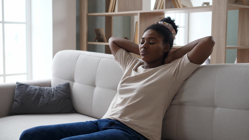 Young, peaceful African-American woman is resting on the couch with her eyes closed after a hard day's work. The concept of rest and tranquility. Royalty-Free Stock Footage #1097417323