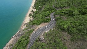 Aerial video of drone flying forward and camera paning up showing tropical road with beaches and mountains in Far North Queensland