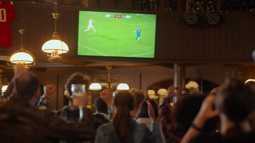 Group of Soccer Fans Watching a Live Football Match in a Sports Bar. People Standing in Front of a TV, Cheering for Their Team. Player Scores a Goal and Crowd Celebrate Winning the Championship. Royalty-Free Stock Footage #1097419537