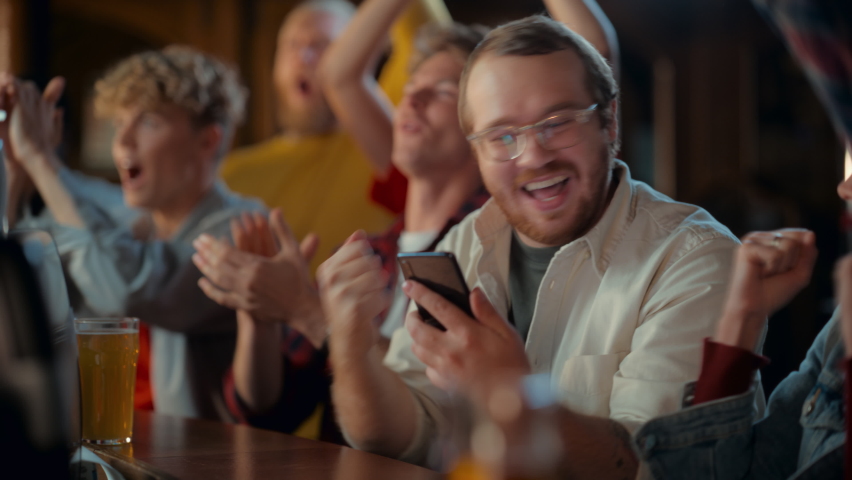 Portrait of a Happy Young Man Holding a Smartphone, Anxious About the Sports Bet on a Soccer Match. Looking at the Screen While Sitting at a Counter, Getting Very Emotional After Winning the Bet. | Shutterstock HD Video #1097419567