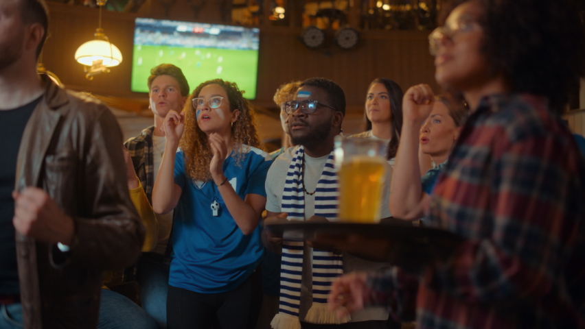 Group of Soccer Fans with Painted Faces Cheering, Screaming, Raising Hands and Jumping During a Football Game Live Broadcast in a Sports Pub. Player Scores a Goal and Friends Celebrate.