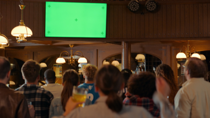 Group of Multicultural Friends Watching a Live Sports Match on TV with Green Screen Display in a Bar. Happy Fans Cheering and Shouting, Celebrating When Team Scores a Goal and Wins the Tournament. Royalty-Free Stock Footage #1097419609
