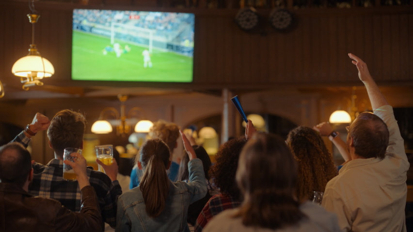Group of Soccer Fans Cheering, Screaming, Raising Hands and Jumping During a Football Game Live Broadcast in a Sports Pub. Player in Blue Shirt Scores a Goal and Friends Celebrate. Slow Motion Footage Royalty-Free Stock Footage #1097419629