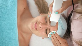 Vertical video of beautician therapist applying face treatment in beauty salon to young woman.