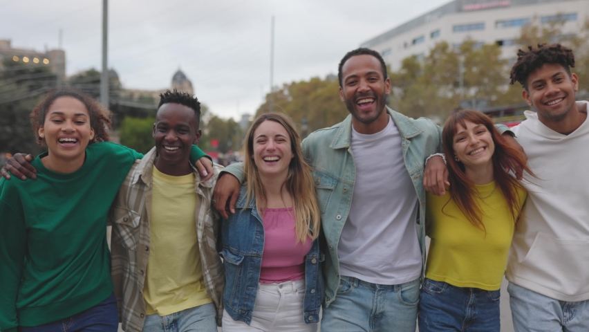Front view group of young people hugging each other walking together smiling at camera outdoors. Friendship, happiness and team concept