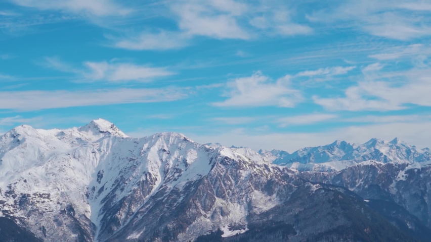 Snow covered Himalayan mountain peaks in front of blue sky with clouds at Manali in Himachal Pradesh, India. Winter landscape with snow capped mountain under sunlight. Snowy winter background.  | Shutterstock HD Video #1097423815