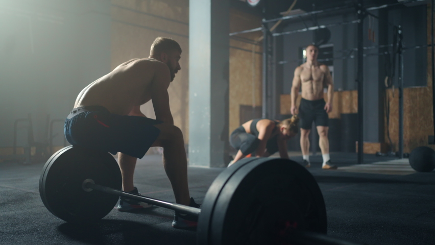 tired bodybuilders resting after workout in gym, men and women are breathing and relaxing muscles