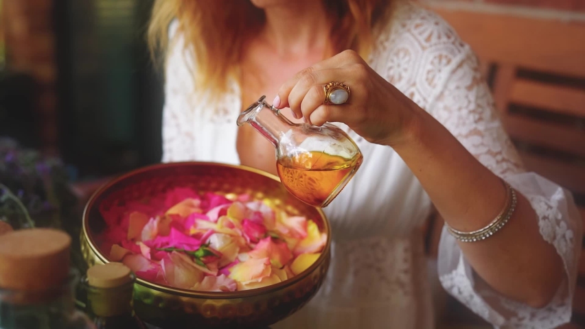 Rose flower and essential oil. Spa and aromatherapy. Woman pours essential oil into a beautiful brass bowl full of flowers. | Shutterstock HD Video #1097428867