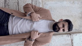 Vertical video of a young bearded man in a jacket and turtleneck looking at his watch and taking his mobile phone out of his pocket to take a call.