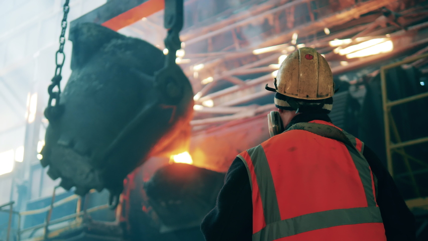 Metallurgist filmed from behind while watching steel casting Royalty-Free Stock Footage #1097435549