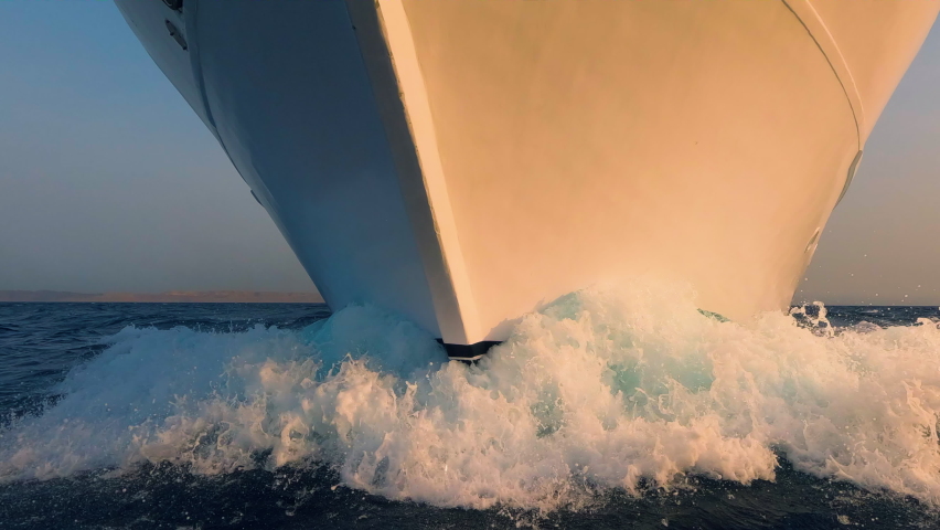 Boat prow and white foam water splashes close up front side view. Yachting, ocean sailing, sunrise sun light on vessel forepart, sailboat bow closeup