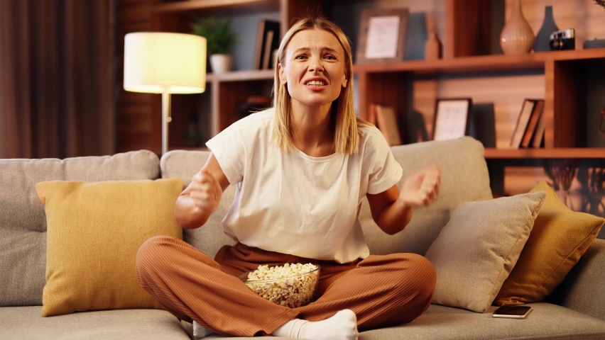 Overjoyed middle aged woman watch sport game and celebrating win goal at home. Blond female fan with a bowl of popcorn enjoying the weekend and cheers for favourite club alone.
