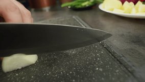 Slow motion close-up video of slicing a white onion with a knife on a cutting board. The chef cooks in the kitchen, the process. High quality 4k footage