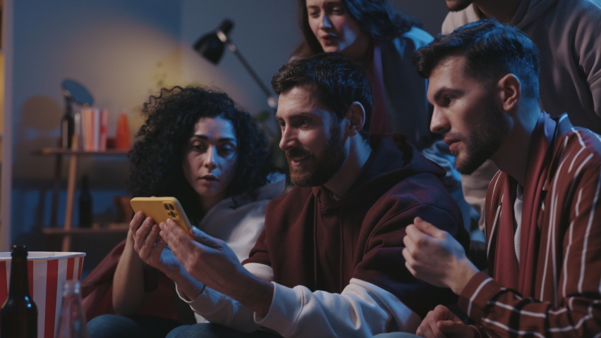 Group of fans sitting on couch and watching football game on smartphone, checking score at home. Online bet, statistics, celebrate when team winning championship | Shutterstock HD Video #1097448047