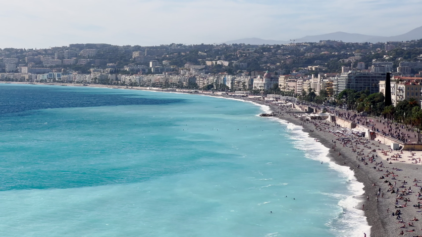 France, Nice, Top view of the famous English promenade with beach on azure sea at sunny day, a sunbathing people in the beach, car traffic, flags different country