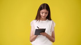 4k video of woman taking down some notes with a pen on yellow background.