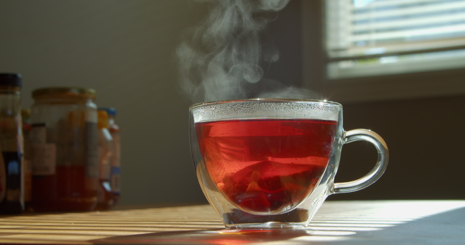 Mug with hot tea on a wooden table in the kitchen. A hand with a small spoon stirs tea in a transparent cup. Slow motion stirring spoon with tea bag.  Royalty-Free Stock Footage #1097451603
