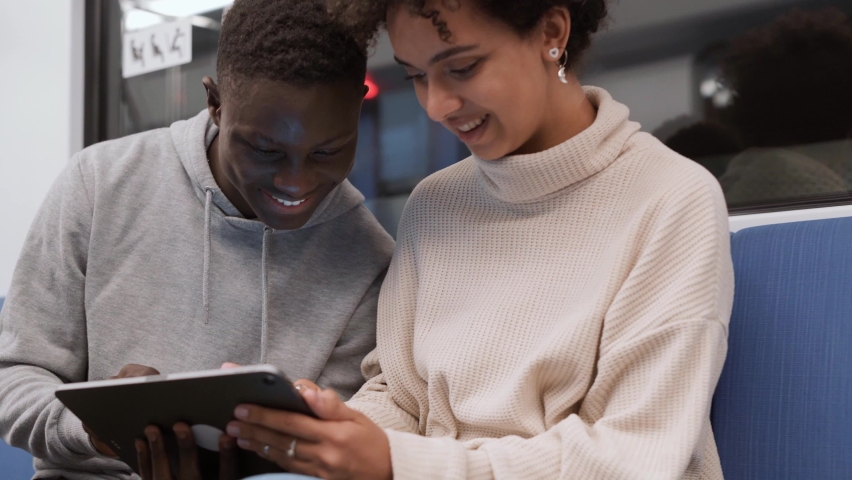 couple of students using a digital tablet while sitting on a subway train.