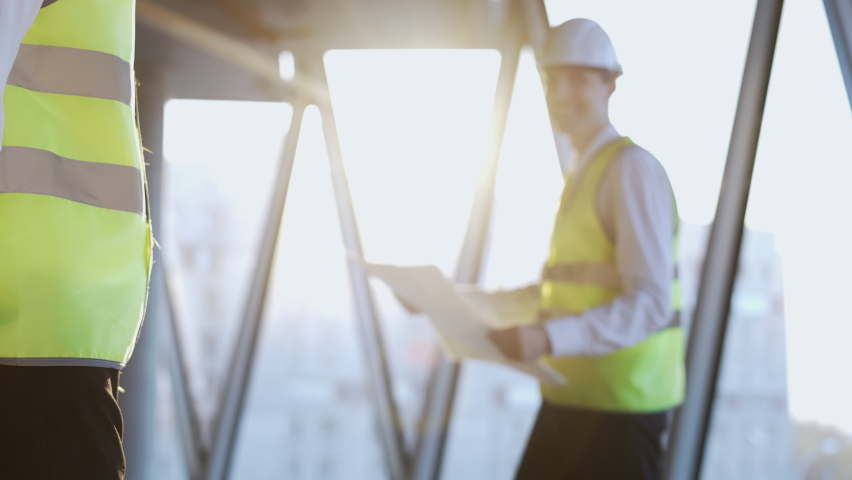 Handshake of colleagues against engineer with project plan smiling near bright panoramic window of skyscraper. Experienced specialists make successful deal standing at construction site close view Royalty-Free Stock Footage #1097453997