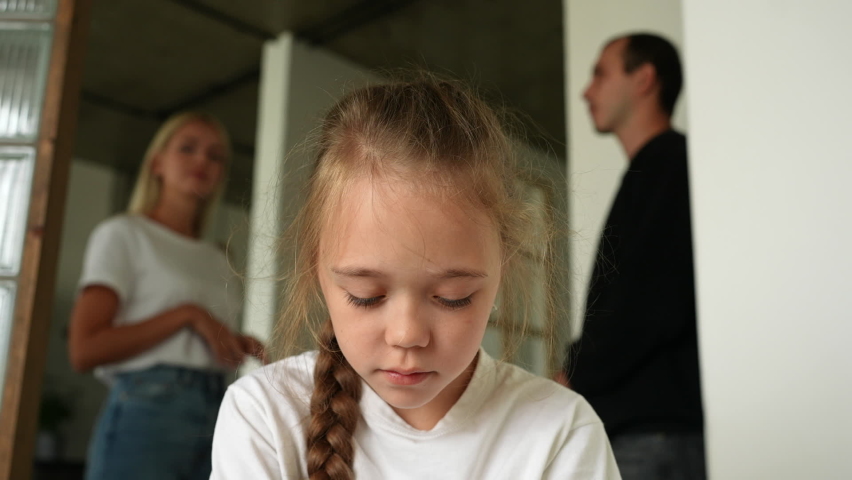 Close-up face of unhappy little daughter suffering looking down stressed and depressed over family problems while angry parents quarrelling and fighting on background at home. Shooting in slow motion. Royalty-Free Stock Footage #1097463263