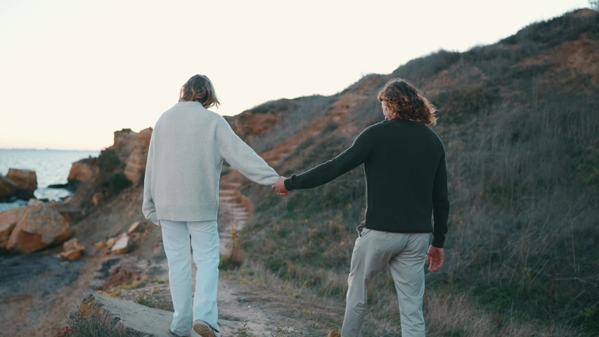 Back view of smiling couple talking and walking on a slope near the sea