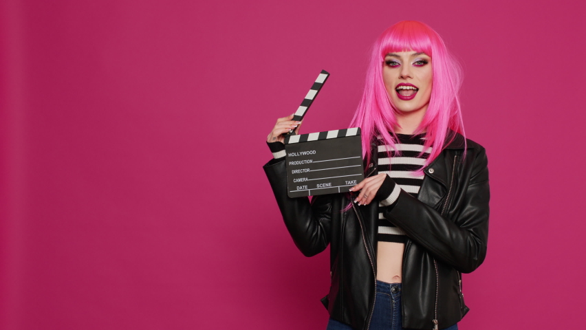 Glamour carefree woman holding film slate and saying action, preparing to record video montage or footage. Young beautiful person with filming equipment, filmmaker over background.