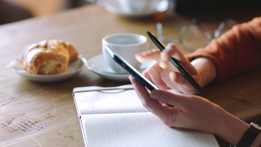 Coffee shop, smartphone and hands with notebook for creative inspiration, social media marketing strategy and remote work planning. Croissant, tea and cafe table and digital writer with writing ideas | Shutterstock HD Video #1097481281
