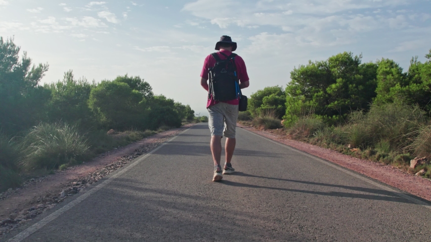 The camera follows a man on a trip or adventure, a young millennial traveler follows the asphalt road to his destination.