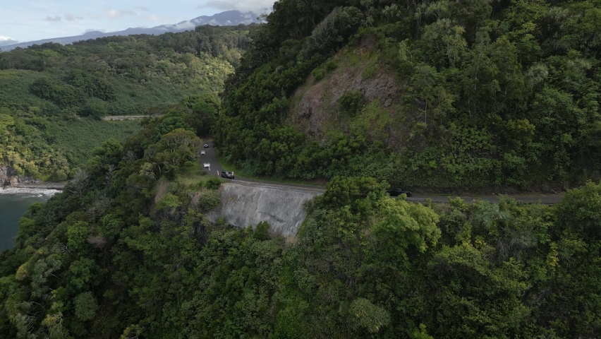 Aerial View Of Cars Driving Along Road To Hana Along Maui Coastline. Pan Left
