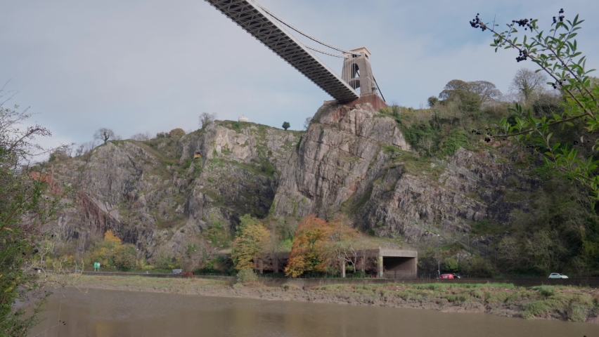 Static slow motion shot. Depicts Bristol Suspension Bridge with the cliffside and traffic below, along with the river Avon.
