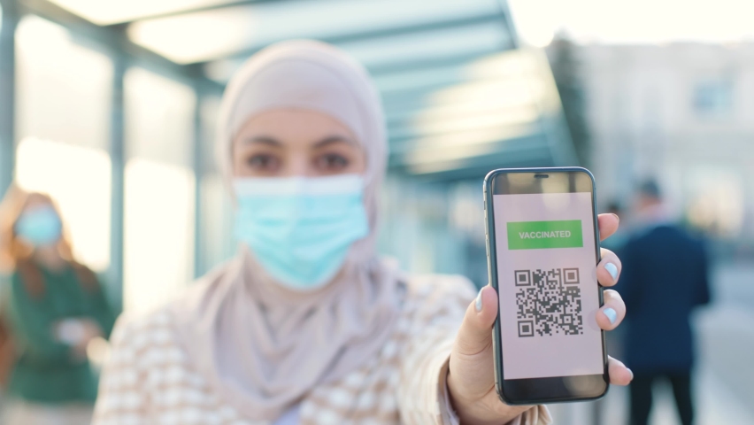 Close up of smartphone screen with vaccination passport QR code. Muslim female in medical mask holding cellphone showing covid vaccine certificate. Vaccinated person, safety travelling concept | Shutterstock HD Video #1097489053