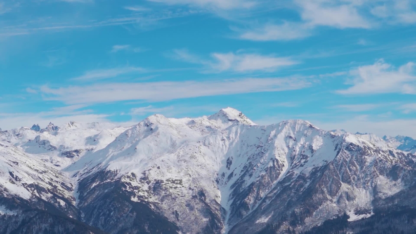 Snow covered Himalayan mountain peaks in front of blue sky with clouds at Manali in Himachal Pradesh, India. Winter landscape with snow capped mountain under sunlight. Snowy winter background.  | Shutterstock HD Video #1097495793