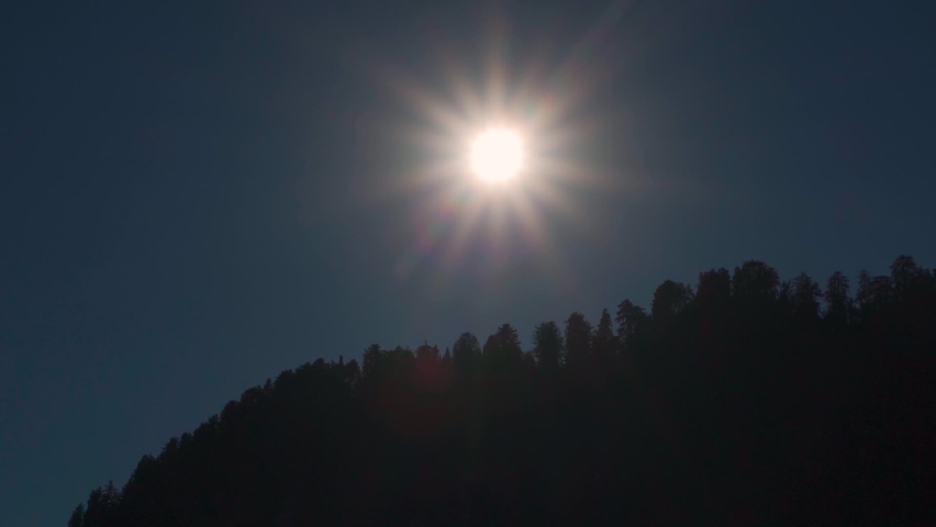View of sun above the trees on the top of the mountain during the noon at Manali in Himachal Pradesh, India. Sun above the mountains in the afternoon with sun stars visible and trees in silhouette.  | Shutterstock HD Video #1097495803