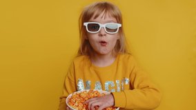 Excited young toddler school girl in 3D glasses eating popcorn, watching interesting tv serial, sport game, film, online social media movie content. Teen female child kid on studio yellow background