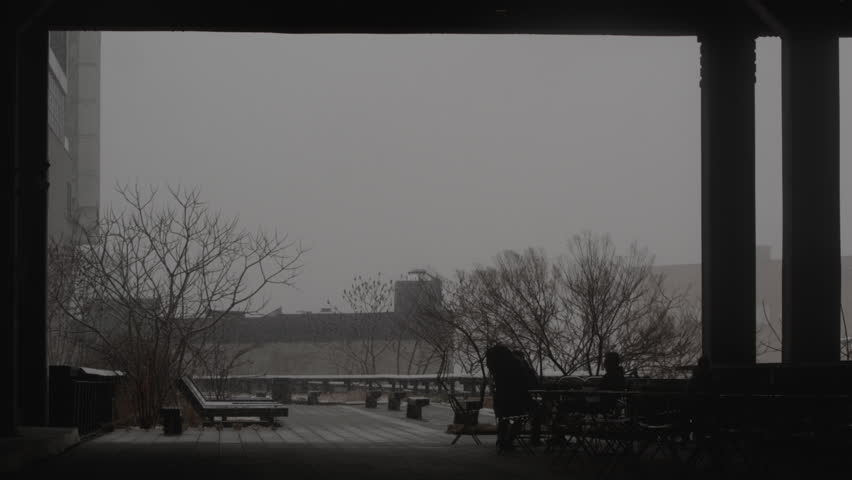 B-roll of light snowfall while friends sit on patio in foreground.