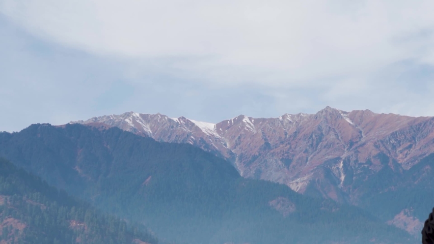 View of the mountain peaks as seen from Naggar near Manali in Himachal Pradesh, India. Natural mountain background. Little snow on the top of the mountain peak during the summer season.  | Shutterstock HD Video #1097500639