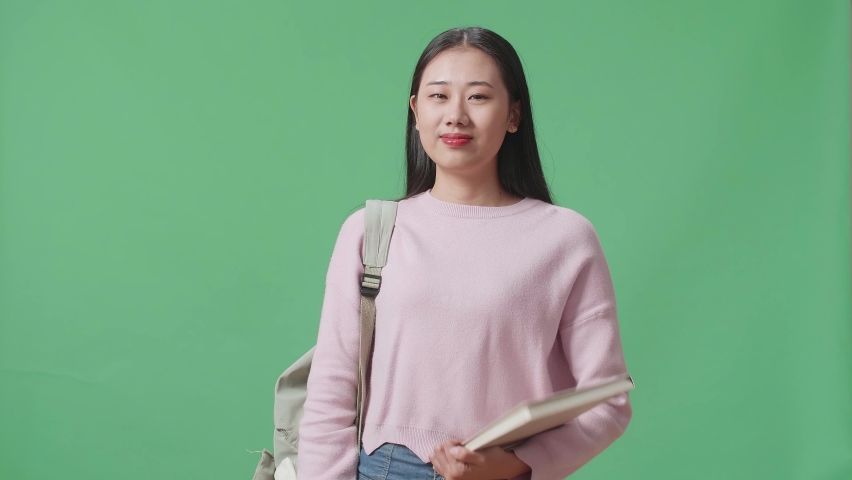 Asian Woman Student Holding Book And Showing Ok Gesture On Green Screen Studio
