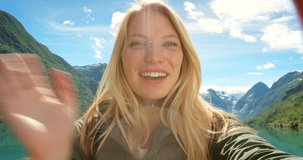 Selfie, woman on video call and mountain travel holiday by lake, waving and blowing kiss at camera for remote chat. Nature freedom adventure, happy vacation videocall and German girl tourist outdoors